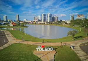 Vista panorâmica da cidade com lago urbano, parque bem cuidado e edifícios modernos ao fundo, destacando o potencial dos imóveis em Toledo PR.