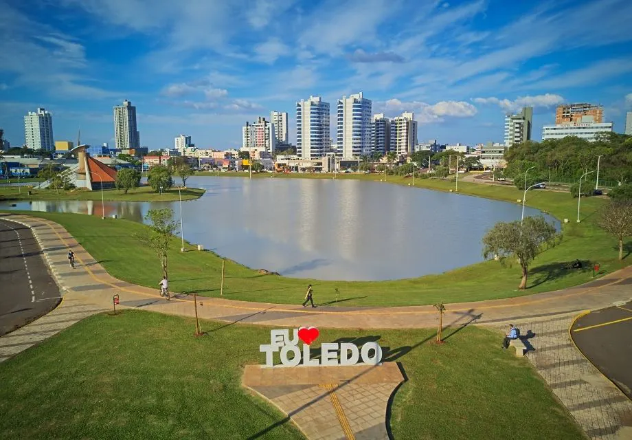 Vista panorâmica da cidade com lago urbano, parque bem cuidado e edifícios modernos ao fundo, destacando o potencial dos imóveis em Toledo PR.