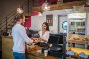 Atendimento em cafeteria de bairro com cliente recebendo café no balcão, representando a força dos negócios de bairro.